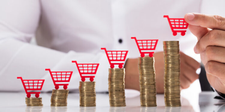 Businessperson's hand placing red shopping cart over increasing stacked coins