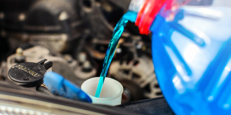Detail on antifreeze car screen wash liquid pouring into dirty car from blue and red anti freeze water container.