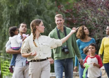 Multi-ethnic tourists with young children (3 to 7 years) visiting a park, walking with tour guide.  Focus on guide.