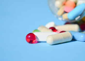 Multicolored bright various type pills and capsules spilling out of a toppled white pill bottle. Colorful pills and tablets on blue background. Pills medicines recall