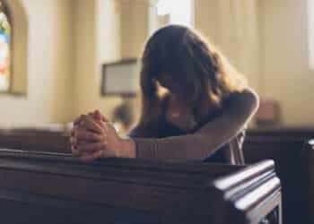 A young woman is sitting with her hands folded and is praying in a church