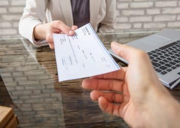 Close-up Of A Business Woman Giving Cheque To Her Colleague At Workplace In Office