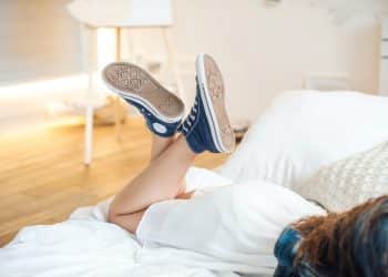 Legs of a girl in denim sneakers and a white skirt, lies on a bed in a room.
